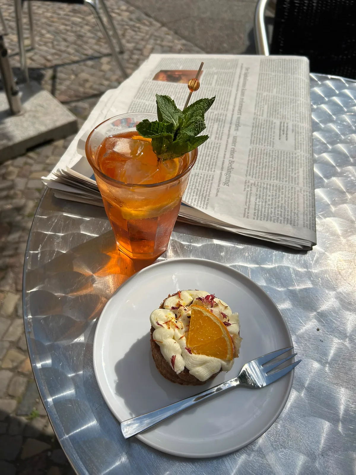 Aperol und ein kleines Törtchen auf dem Tisch vor dem Café