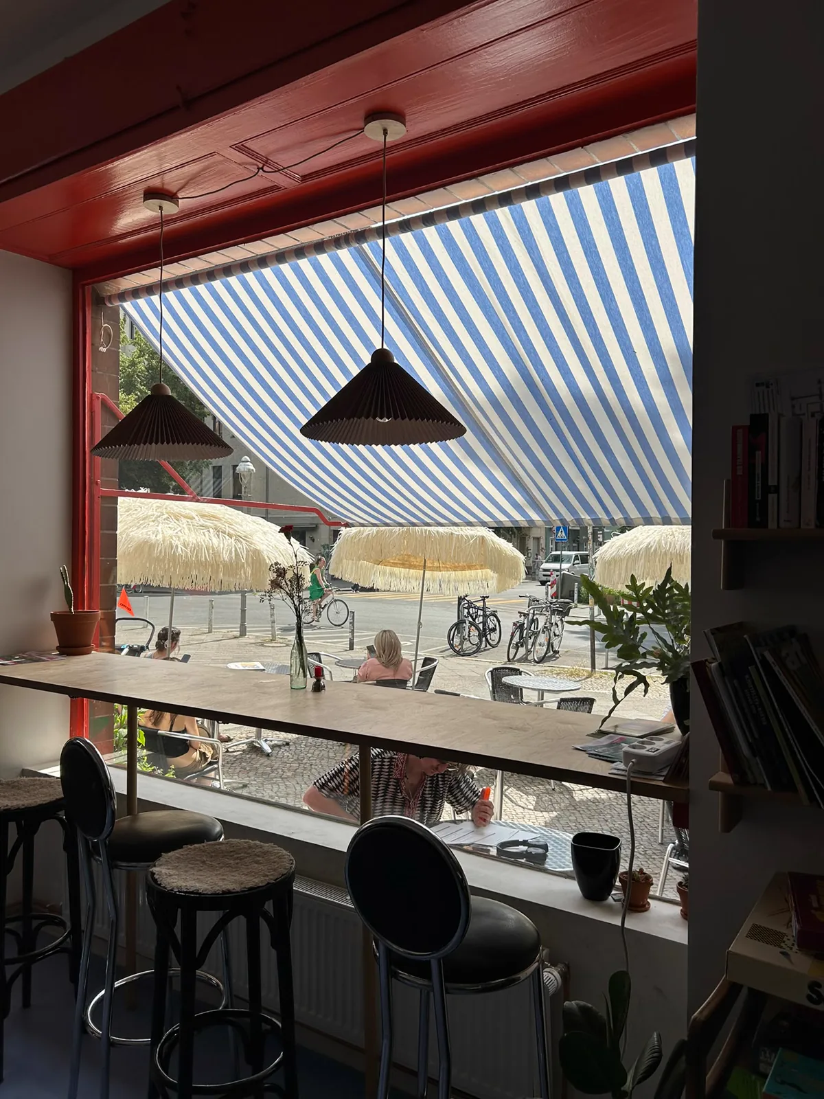 Blick durch das große Fenster auf Markise und Außentische